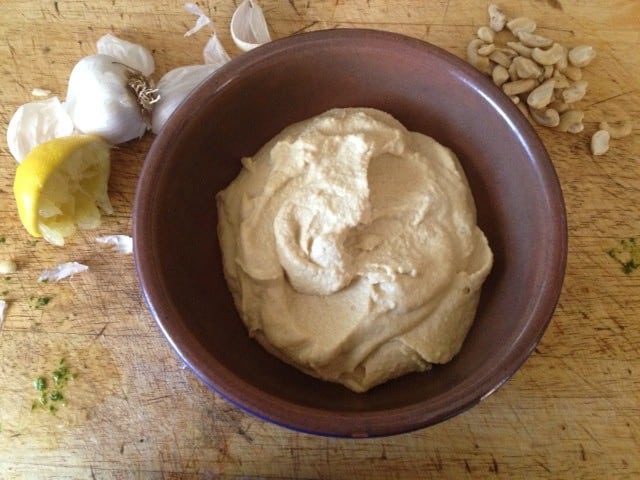 a bowl of cashew cheese sauce with garlic, cashew nuts and squeezed lemon scattered around it 