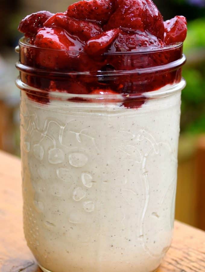 a big jar of vegan cashew cream topped with roasted strawberries