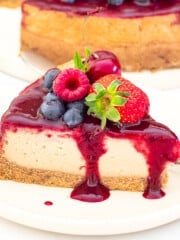 a slice of vegan New York cheesecake topped with berry compote and fresh berries on a plate