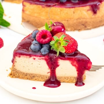 a slice of vegan New York cheesecake topped with berry compote and fresh berries on a plate