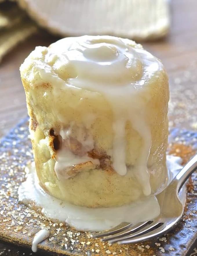 A cinnamon roll in a mug turned out on a plate with dribbly frosting