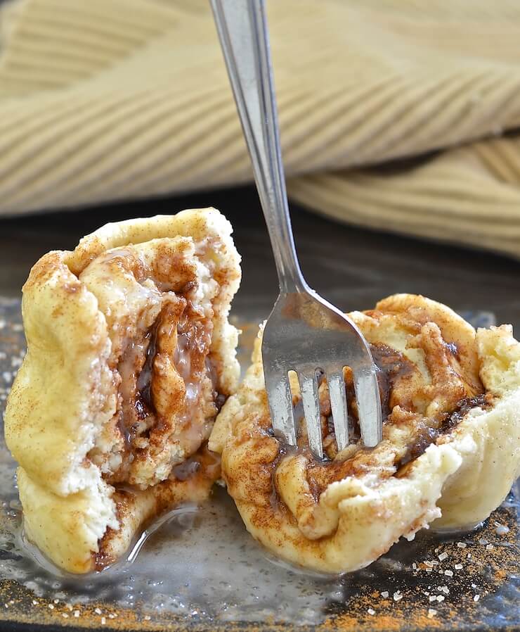 cinnamon roll in a mug turned out and cut in half with a fork stuck in one half 