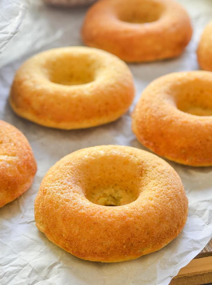 naked orange olive oil baked donuts laid out on baking parchment ready to be drizzled with frosting