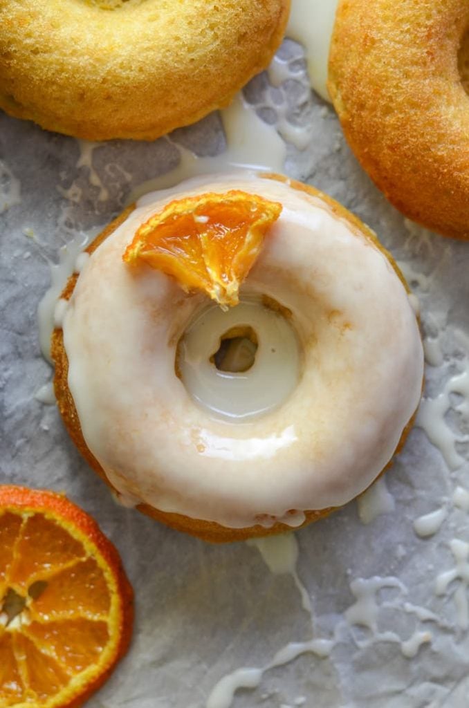 close-up orange olive oil baked donuts with frosting and candied orange wedge