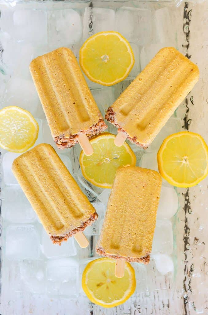 Creamy Lemon Cheesecake Pops laid on a bed of ice with sliced lemon
