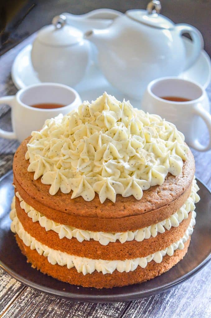 Layered Earl Grey Vegan Cake with Lemon Frosting in foreground with white tea set in background