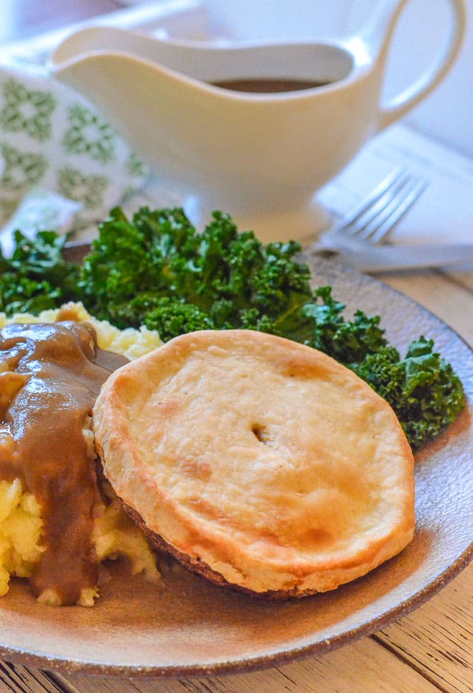 Individual Easy Vegan Mushroom Pie on a plate with mashed potato, kale & gravy