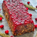 Mushroom Lentil Loaf with Cranberry topping turned out on a slate board and surrounded by scattered cranberries and rosemary