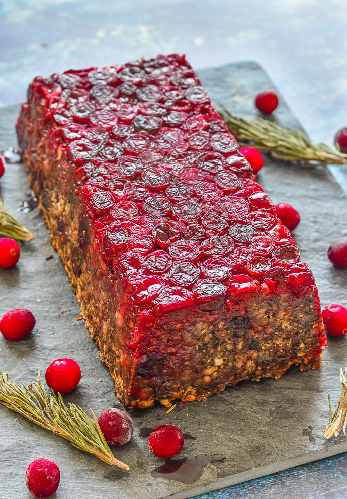 Mushroom Lentil Loaf with Cranberry topping turned out on a slate board and surrounded by scattered cranberries and rosemary