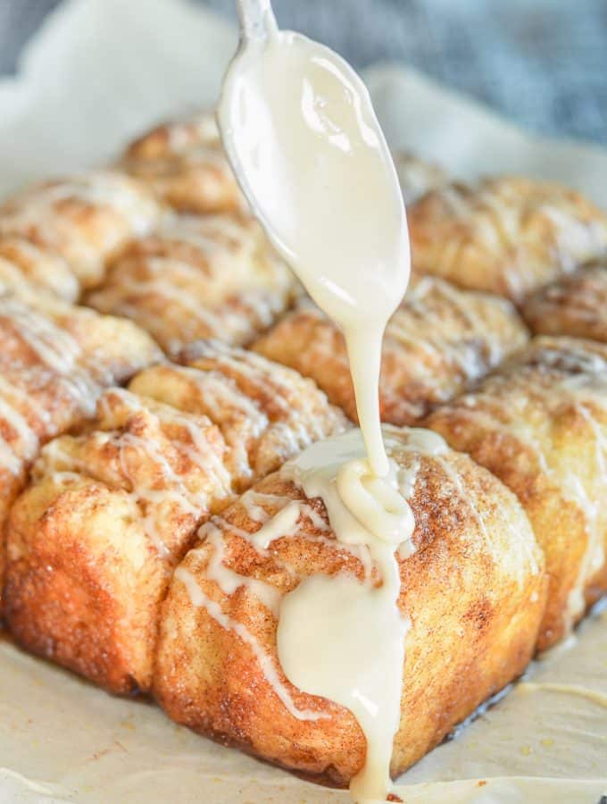 Frosting dribbling off a spoon onto freshly baked No Knead Cinnamon Pull Apart Bread