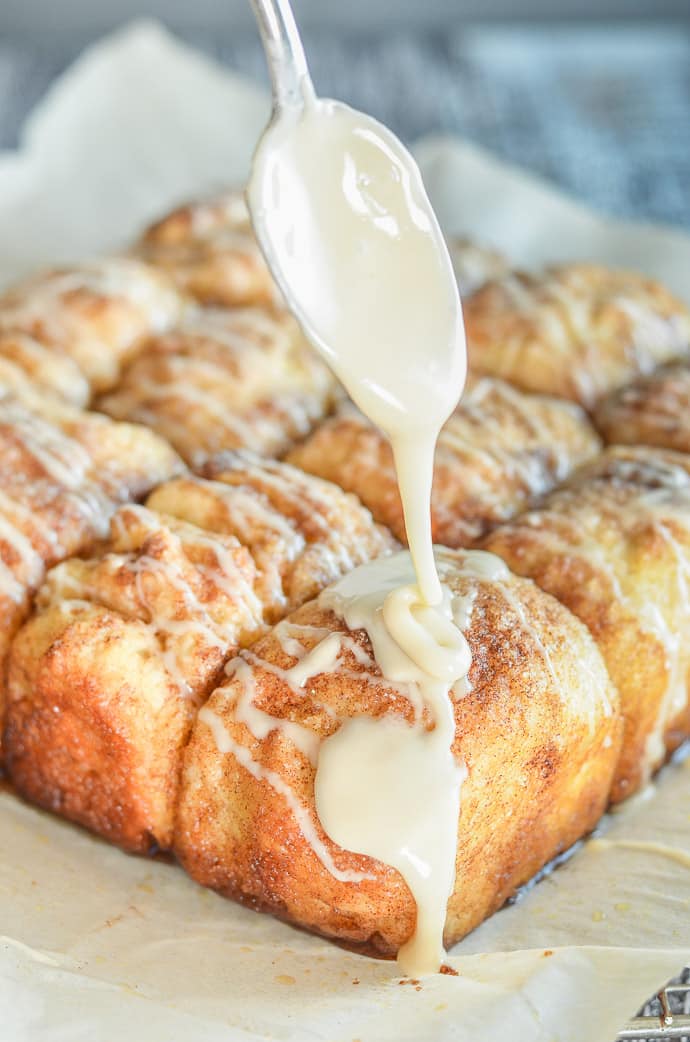 Frosting dribbling off a spoon onto freshly baked No Knead Cinnamon Pull Apart Bread