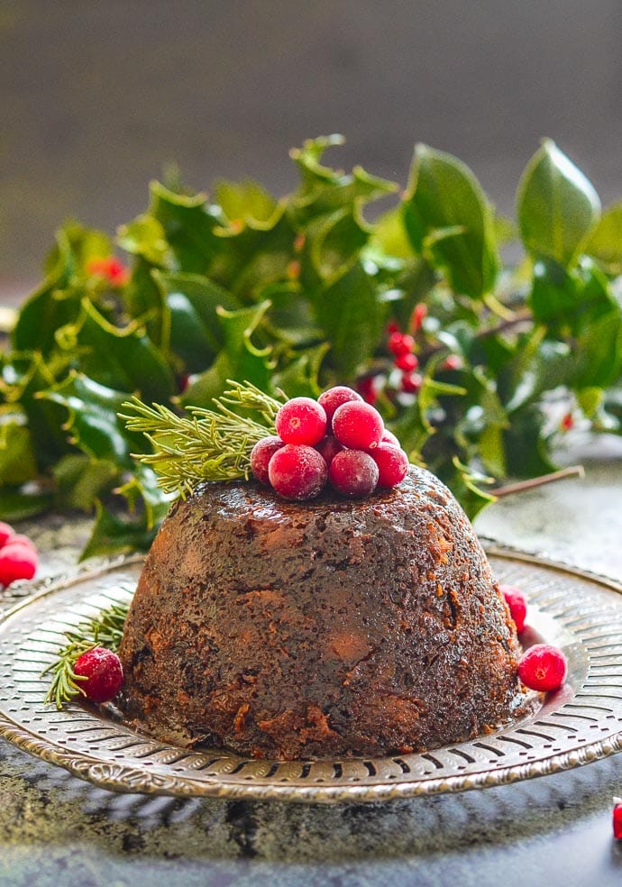 Vegan Christmas Pudding turned out onto metal plate and topped with frosty cranberries and fresh rosemary