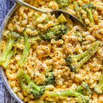 a close up shot of dairy free mac and cheese with broccoli in a stainless steel pan and scattered with lots of fresh ground black pepper