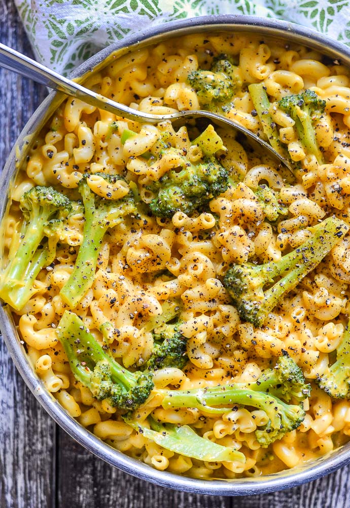 a close up shot of dairy free mac and cheese with broccoli in a stainless steel pan and scattered with lots of fresh ground black pepper