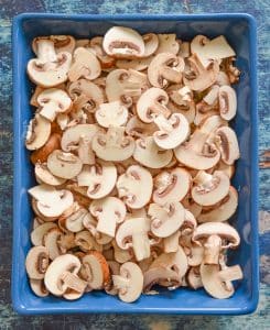 sliced mushrooms over dried rice, onions and garlic in a blue dish - the 3rd step in making Easy Oven Baked Garlic Mushroom Rice