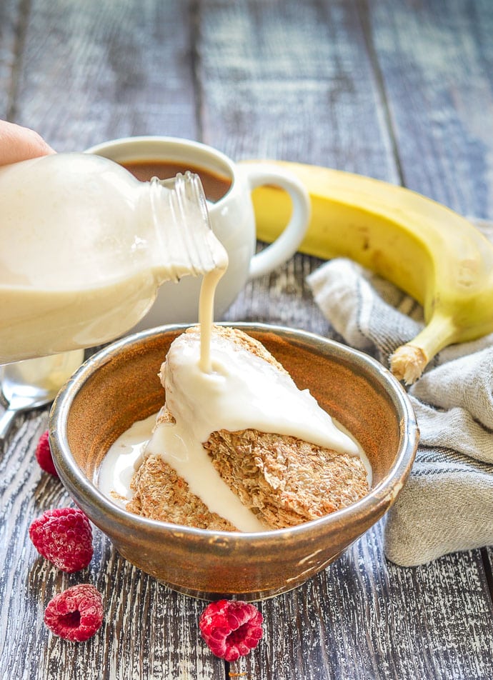 oat milk being poured from bottle onto cereal in a bowl