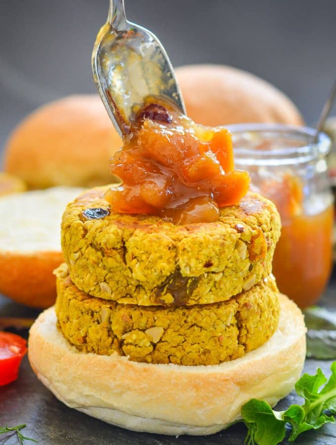 two curried chickpea burgers stacked on a bun with a generous spoon of mango chutney being dolloped on top
