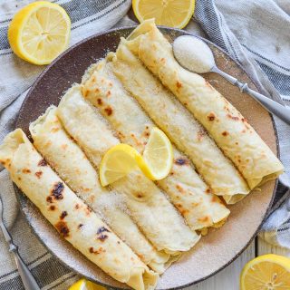 Vegan English Pancakes rolled on a plate and topped with sugar and lemon