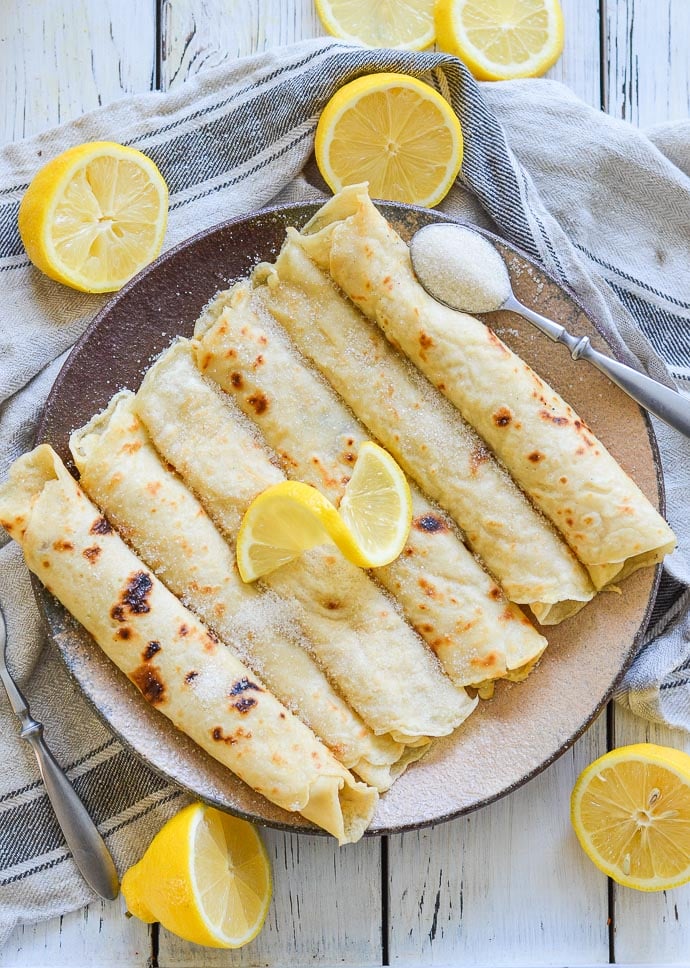 Vegan English Pancakes rolled on a plate and topped with sugar and lemon