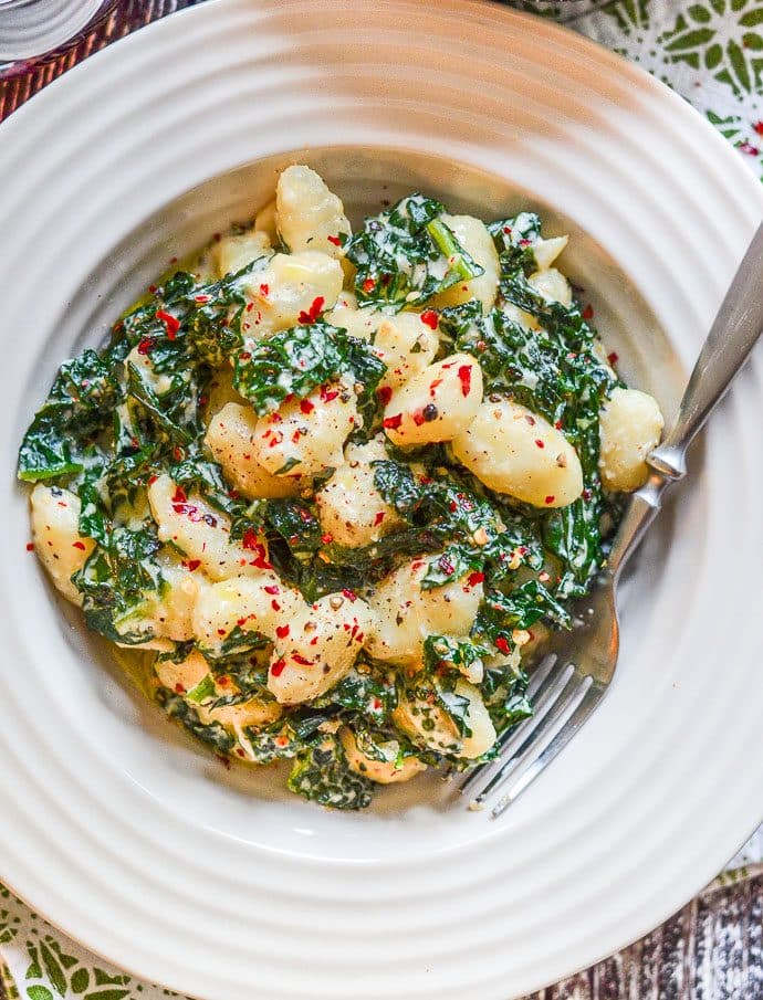 Vegan gnocchi and kale in a creamy sauce inside a bowl. Photograph taken from above.