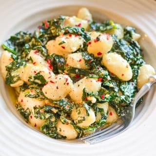 Vegan Gnocchi and kale in a creamy sauce and sprinkled with red pepper flakes and freshly ground black pepper