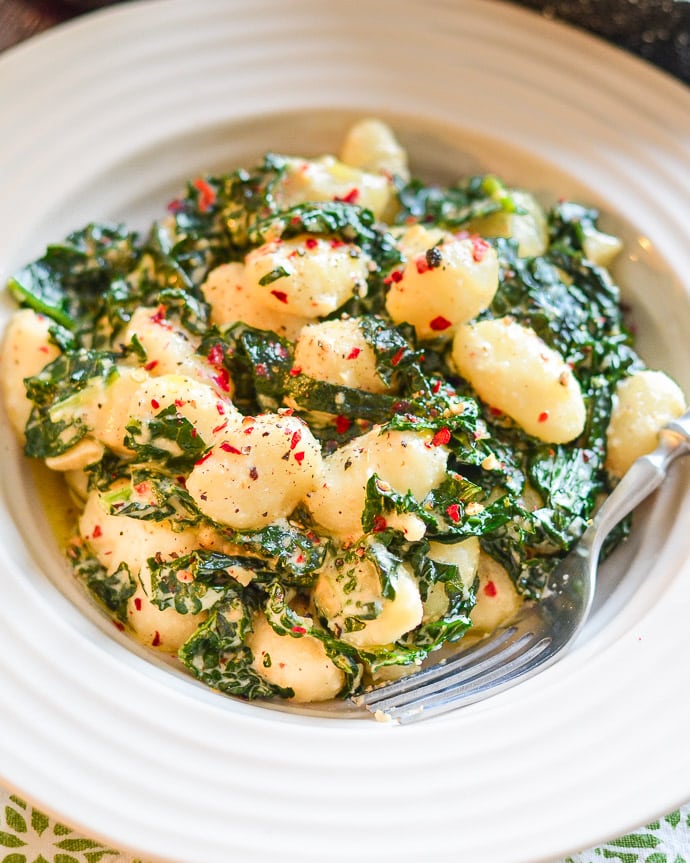 Vegan Gnocchi and kale in a creamy sauce and sprinkled with red pepper flakes and freshly ground black pepper