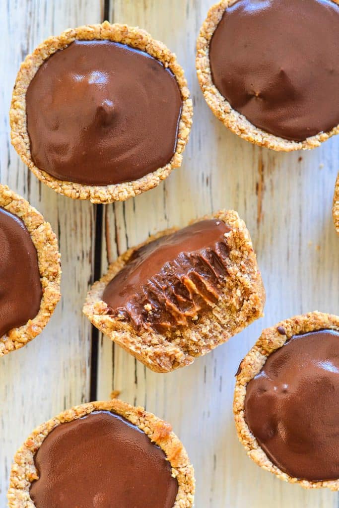 Healthier chocolate carmamel cookie cups on a white board. One with a bite taken out.