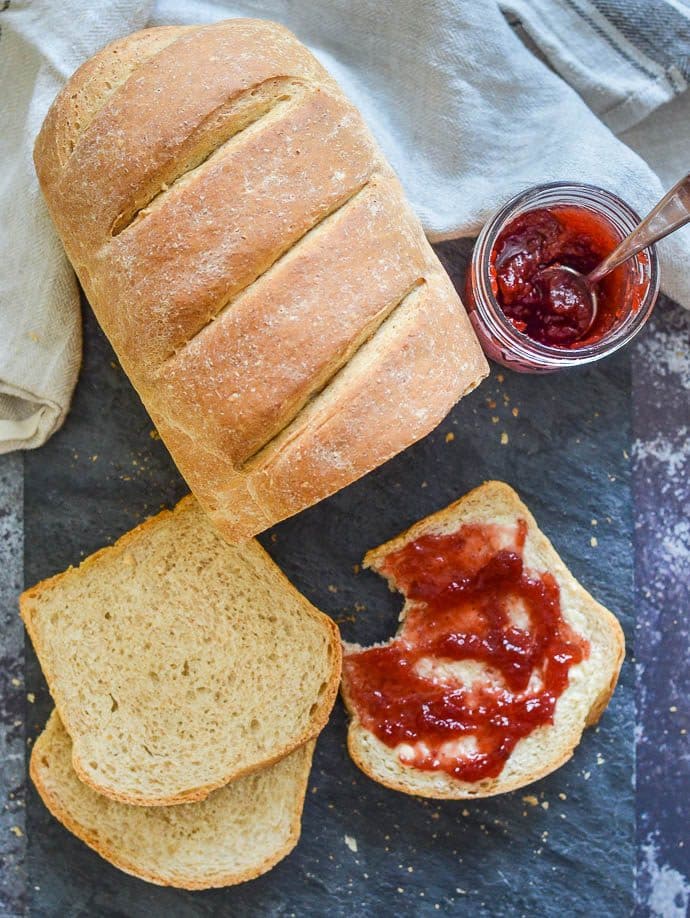 loaf of easy whole wheat bread on slate board, partly sliced and spread with jam
