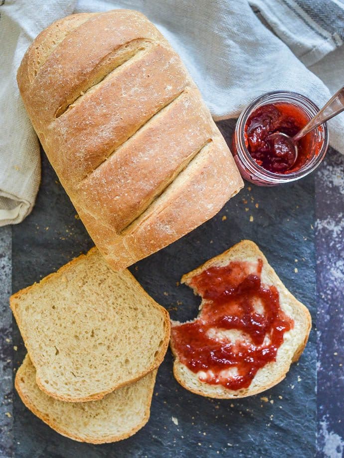 pagnotta di pane integrale facile su tavola di ardesia, parzialmente affettato e spalmato con marmellata