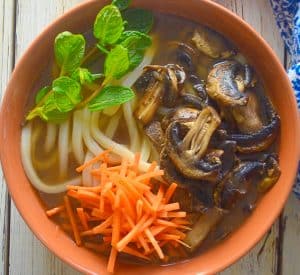 udon noodle soup topped with carrot, mushrooms and mint