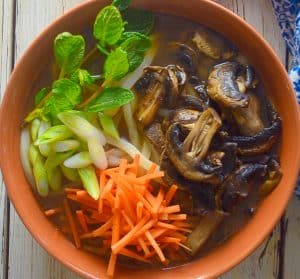 udon noodle soup topped with carrot, mushrooms, mint & green onions