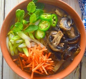 udon noodle soup topped with carrot, mushrooms, mint, green onions and jalapeños