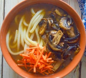 udon noodle soup topped with carrot and mushrooms