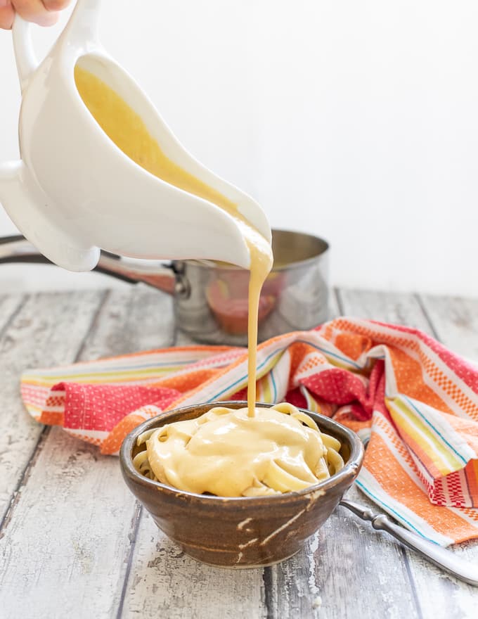 vegan cheese sauce being poured from a jug onto pasta