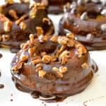 a chocolate dipped vegan pumpkin donuts sprinkled with nuts.