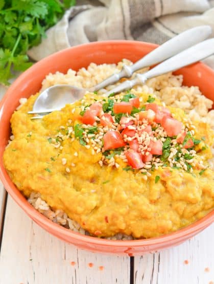 Instant Pot Lentil Dahl served over rice in a bowl with herbs, tomato and nuts sprinkled on top