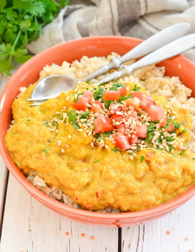 Instant Pot Lentil Dahl served over rice in a bowl with herbs, tomato and nuts sprinkled on top