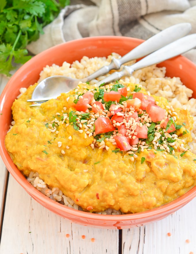 Instant Pot Lentil Dal served over rice in a bowl with a sprinkle of chopped herbs, chopped tomato and chopped cashew nuts