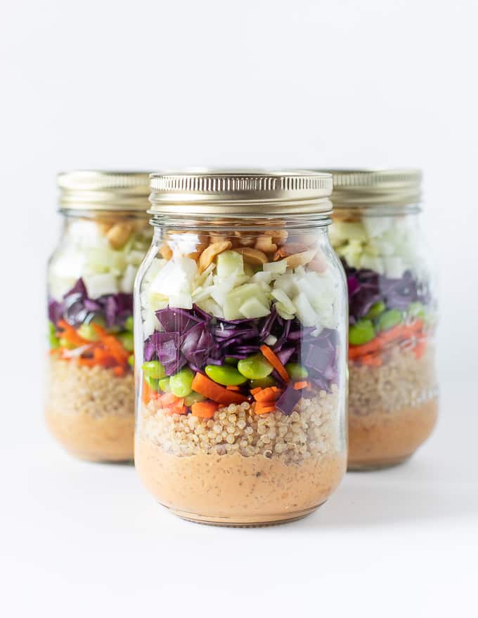 A layered salad in a mason jar. Dressing in bottom then quinoa, carrots, purple cabbage, green cabbage, edamame beans, peanuts all piled on top