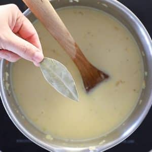 bay leaf being put in a pan of vegan potato soup