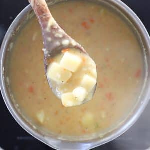 a spoon of chunky vegan potato soup above the pan