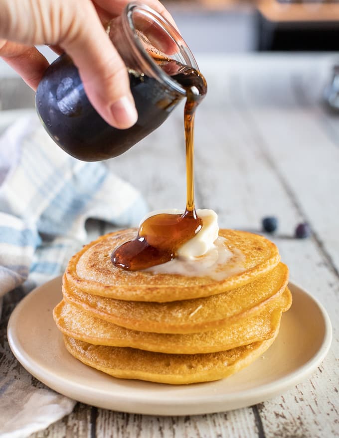 A stack of vegan gluten free pancakes with vegan butter and maple syrup being poured over