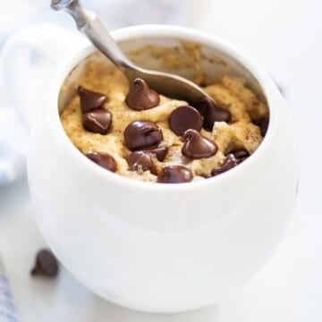 a chocolate chip cookie in a mug with a spoon in it.