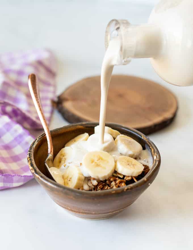 Homemade cashew milk being poured on granola and sliced banana
