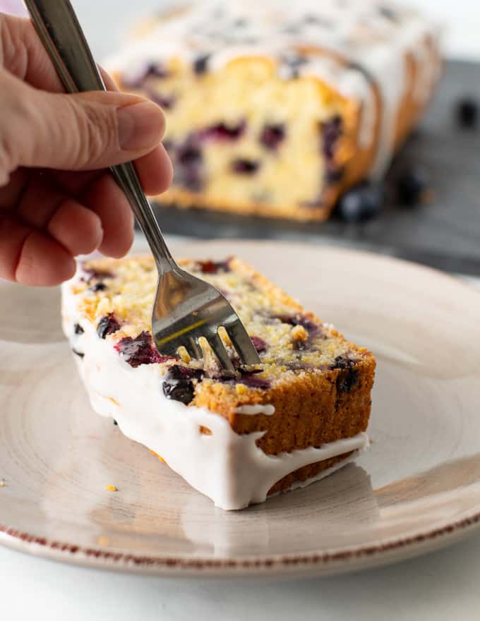 someone sticking a fork into a slice of lemon blueberry loaf