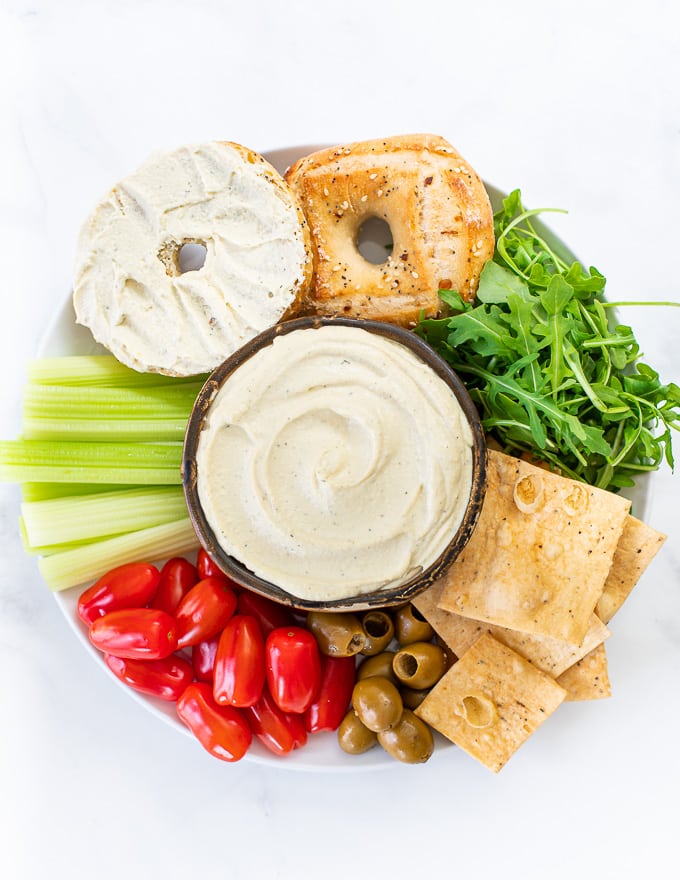 A vegan cream cheese platter with a bowl of vegan cream cheese, crackers, bagels and veggies