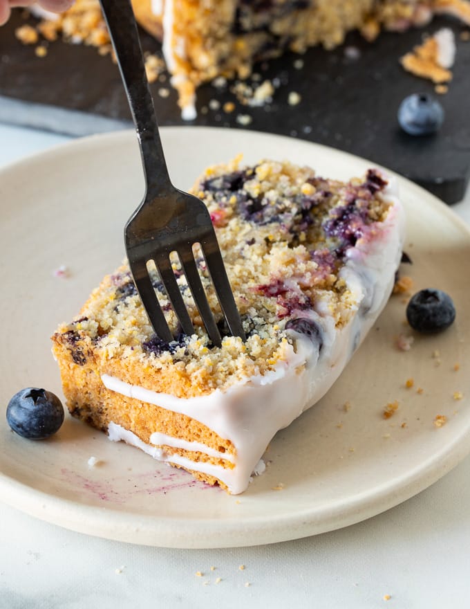 a slice of gluten-free lemon cake on a plate with someone sticking a fork into it 