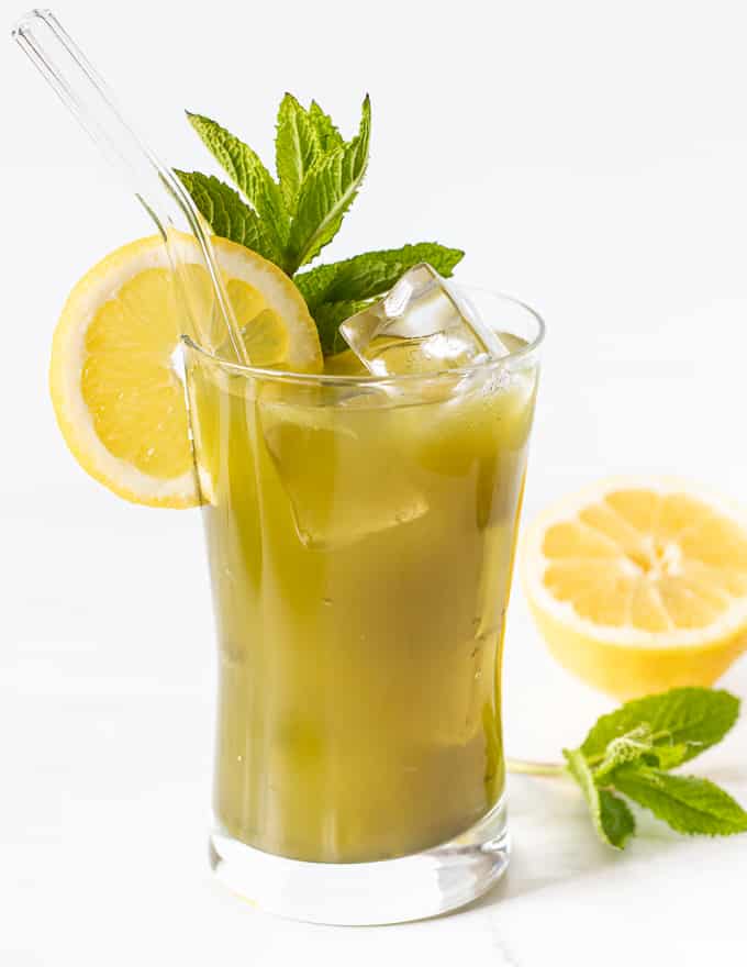 a glass of matcha lemonade garnished with a lemon slice and fresh mint