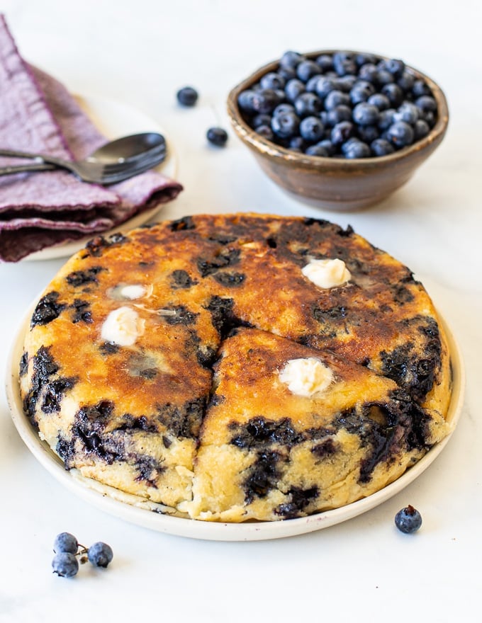 a giant, golden, vegan blueberry pancake on a plate with melted butter