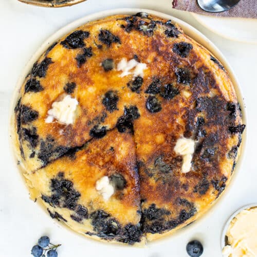 a giant vegan blueberry pancake on a plate with melted butter